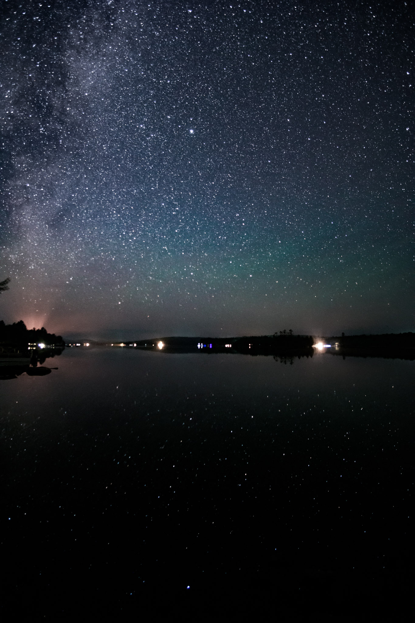 The stars and are reflected in the still lake, the horizon is greenish